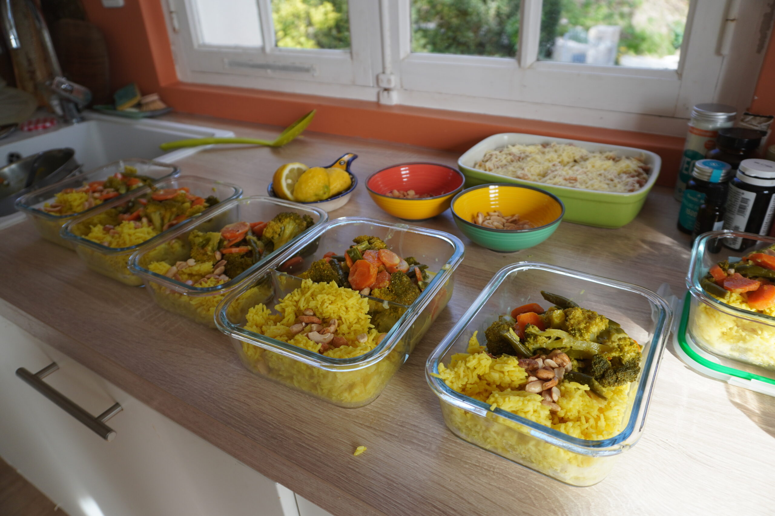 Gros plan sur un curry de légumes vert appétissant préparé en batch cooking servi dans un plat en verre avec une cuillère en bois.