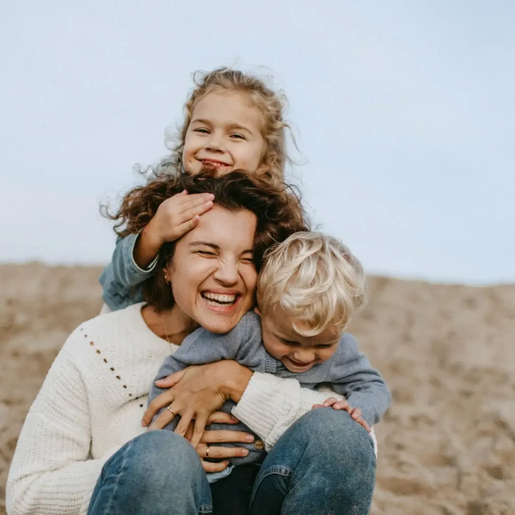 Maman souriante en train de jouer avec ses deux jeunes enfants, illustrant la construction du lien d'attachement au quotidie