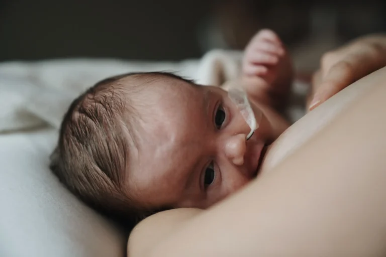 Gros plan d'un bébé prématuré avec sonde naso-gastrique contre sa maman lors d'une tétée.
