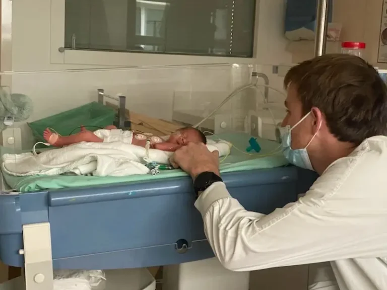 Papa veillant sur son bébé prématuré installé dans une couveuse en néonatalogie.