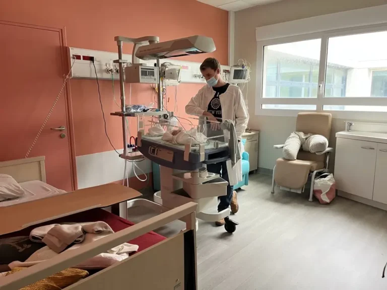 Chambre d'hôpital aménagée en nid de maternage avec le papa veillant sur son bébé prématuré.